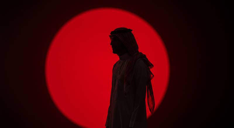 A silhouetted figure in a shemagh standing before a red circle of light